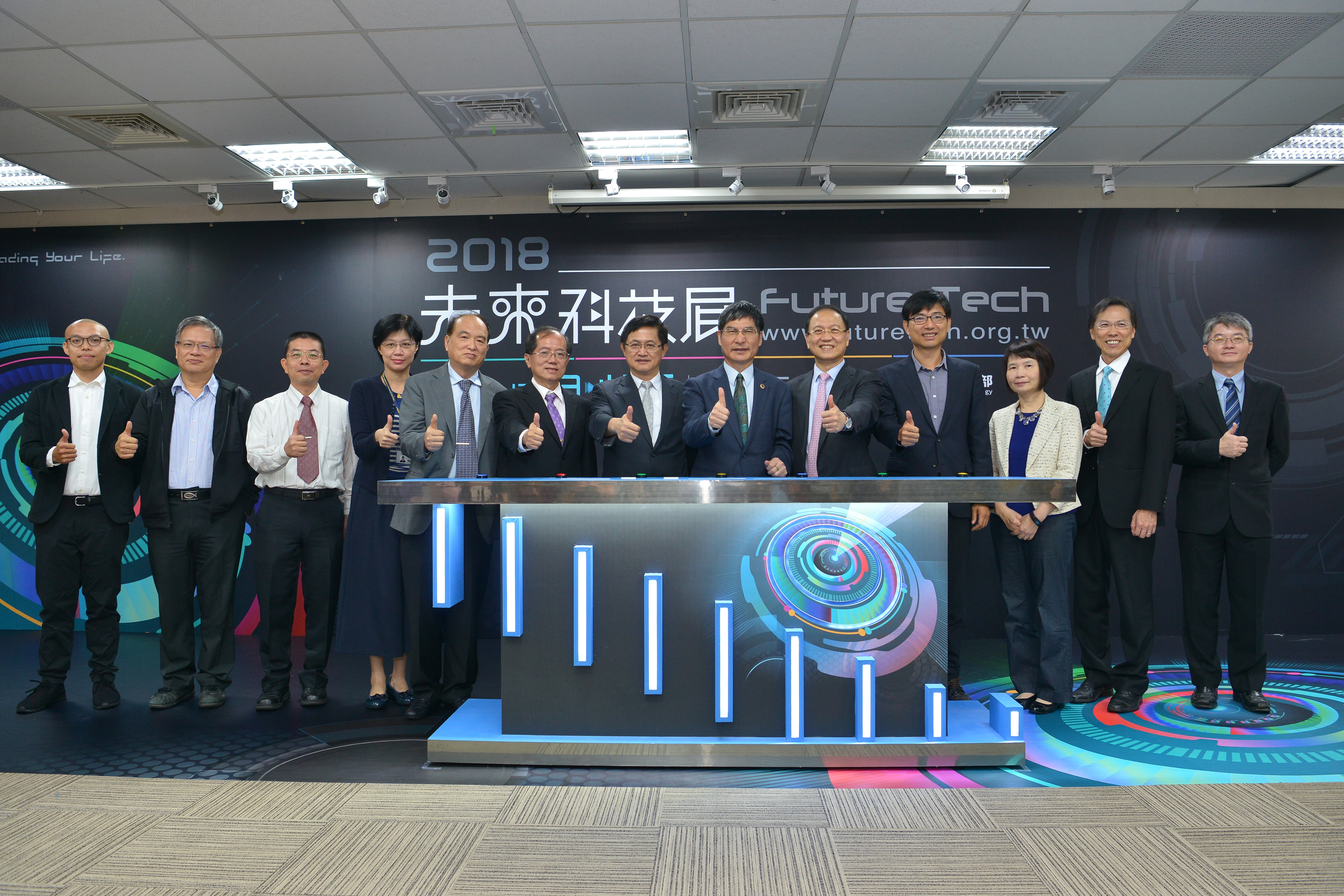 科技部部長陳良基與出席貴賓及研究團隊共同宣示2018未來科技展正式啟動，合照左起為中研院特聘研究員蔡定平研究團隊代表「可見光寬頻消色差介電質超穎透鏡成像」、國立清華大學教授江安世「多尺度生物顯微影像技術」、國立中正大學教授高永洲「機械加工單元作動量測暨虛擬實境視覺化模擬應用」、科技部前瞻及應用科技司司長楊琇雅、國立交通大學副校長張翼、國立清華大學副校長陳信文、台北市電腦公會理事長童子賢、科技部部長陳良基、台灣生物產業發展協會理事長李鍾熙、科技部產學及園區業務司司長邱求慧、科技部人文及社會科學研究發展司司長鄭毓瑜、中國醫藥大學教授卓夙航「干擾性RNA藥物用於治療近視」、國立臺灣大學教授林沛群「多地形上輪腳複合移動載台技術」